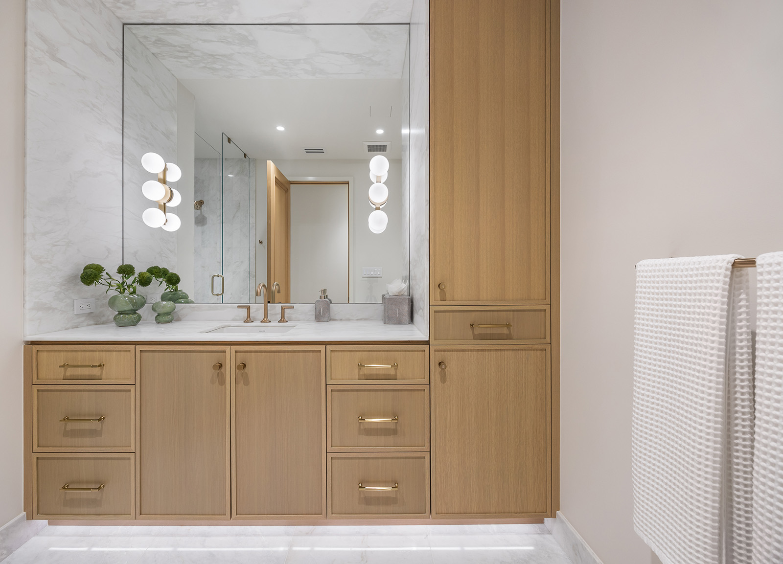 Bathroom remodel in Dallas by Renowned Group single oak vanity with marble backsplash and gold sconces